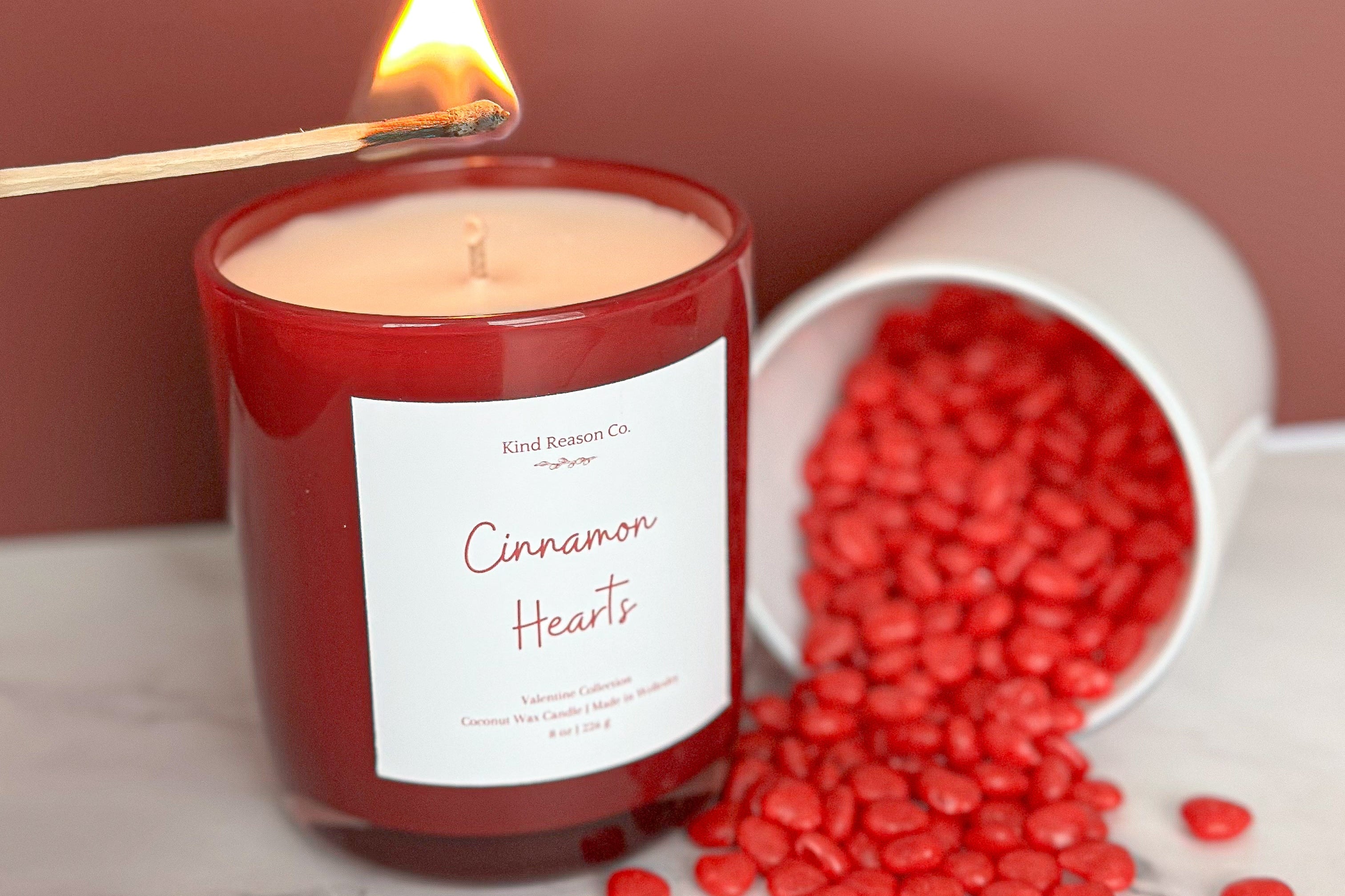 Candle labeled 'Cinnamon Hearts' with red heart-shaped candies on a marble surface.